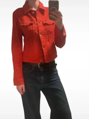 Tiger of Sweden röd croppad jeansjacka - Snygg röd jeansjacka från Tiger of Sweden Jeans, i italienskt premiumdenim från Candiani. Klassisk modell med krage, knappar framtill och två bröstfickor. Jackan är croppad och har långa ärmar.