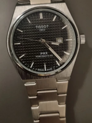 Svart herrklocka - Säljer en stilren klocka med svart urtavla och datumfönster. Klockan har ett klassiskt armband i borstat rostfritt stål och safirglas. Snyggt rutmönster på tavlan och tydliga indexmarkeringar. Perfekt accessoar för dig som gillar tidlös design.