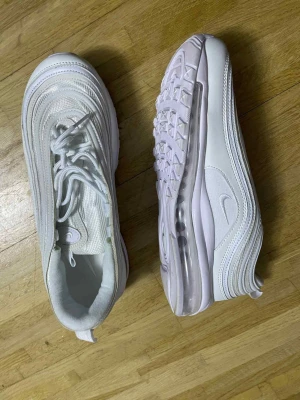 Nike Air Max 97 helvita sneakers - Säljer ett par Nike Air Max 97 sneakers i helvitt med snygga vågiga linjer och synlig Air-sula. Skorna har snörning, rund tå och är tillverkade i syntet och mesh för en fräsch och sportig look. Perfekta för dig som gillar klassiska och cleana sneakers.