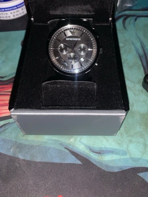 Armani Klocka - Bilderna visar en svart klocka från Emporio Armani i sin originalask, men ingen väst syns på bilderna.