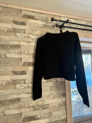 Svart croppad stickad tröja Divided - Säljer en svart croppad stickad tröja från Divided. Tröjan har ribbad struktur, rund halsringning och långa ärmar. Perfekt till höst och vinter för en chill och snygg look.