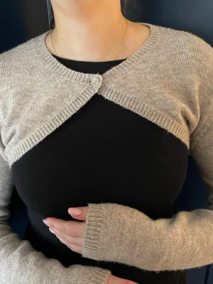 Beige stickad kofta från Gina Tricot - Säljer en beige stickad kofta från Gina Tricot i storlek S. Koftan är kort och har en knapp framtill vid halsen - med långa ärmar🧡