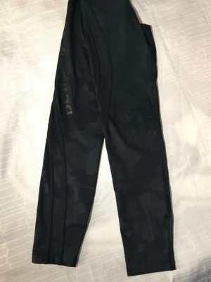 Better Bodies svarta camo leggings S - Snygga svarta leggings från Better Bodies med diskret camomönster och logga längs benet. Tight passform och stretchigt material som passar perfekt till gymmet eller träning. Hög midja för extra komfort och stöd.