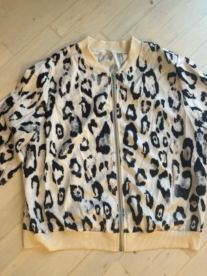 Leopardmönstrad tröja med dragkedja - Säljer en cool leopardmönstrad  tunn tröja  i vitt och svart med beige ribbade muddar och krage. Tröjan  har dragkedja framtill och är perfekt för dig som vill sticka ut med ett djuriskt print. Passar till både chill och lite mer edgy outfits.