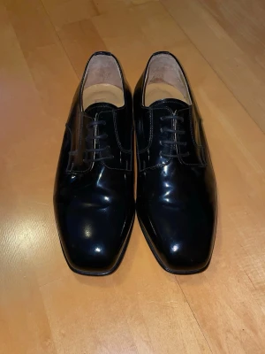 Svarta skinnskor från Via Verdi - Säljer ett par svarta skinnskor från Via Verdi. De är gjorda av äkta läder och tillverkade i Italien. Skorna har snörning, platt sula, glasig ovansida, och en snygg fyrkantig tå. Insidan är i ljust skinn och yttermaterialet är slätt och elegant. De är använda kanske en gång inomhus men är fortfarande i bra skick. Det är ett dyrare märke men säljer ändå billigt. Priset är inte hugget i sten. Perfekt för ett lite mer uppklätt tillfälle. Skriv vid frågor!