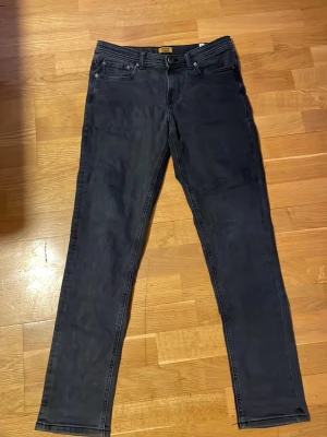 Svarta slim/glenn jack & Jones jeans 170 - Svarta jeans från Jack & Jones i storlek 170, med klassisk femficksdesign och smal passform. Jeansen har bälteshällor, knapp och dragkedja framtill samt raka ben. Perfekta för dig som gillar en stilren och enkel look.