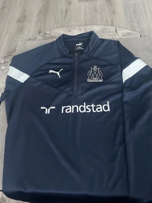 Marseille träningströja - Aldrig använd, alltså helt ny! Skick 10/10 köpt på unisport.se. Träningströja med zip som går att använda i vardagen också! Skön och tunn så luftig vid varmare dagar!