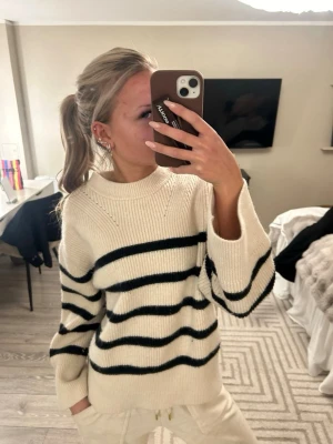 Randig stickad tröja - Säljer en mysig stickad tröja i offwhite med svarta ränder. Tröjan har en relaxed fit, rund halsringning och långa ärmar. 