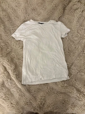 Vit basic t-shirt i bomull - En enkel vit t-shirt med rund hals och korta ärmar. Perfekt för att bygga lager eller köra en clean look. Materialet är mjuk bomull som känns skönt mot huden. Passformen är normal och t-shirten har en klassisk, rak siluett.