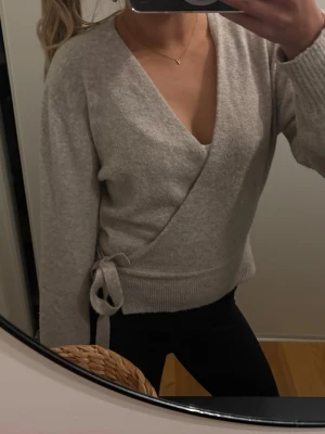 & other stories omlottstickad tröja - Säljer en beige stickad omlott-tröja med knytband i sidan från & other stories. Pyttelite nopprig annars inga tecken på användning 