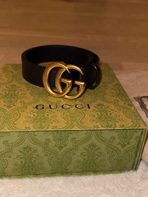 Svart Gucci skärp med GG-spänne - Snyggt svart skärp från Gucci i äkta läder med ikoniskt dubbelt GG-spänne i guld. Perfekt accessoar för att lyfta vilken outfit som helst och ger en lyxig touch. Klassisk design som aldrig går ur tiden.