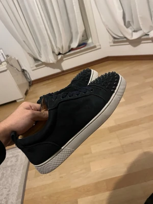 Mörkblå sneakers med nitar - Säljer ett par sneakers med nitar på tån och vit sula. Skorna har snörning och är tillverkade i mocka för en lyxig känsla. Perfekta för dig som vill sticka ut med din stil. 2 stycken nitar fattas, men en extra nit finns som kan skickas med och bara limmas på. Ingen box