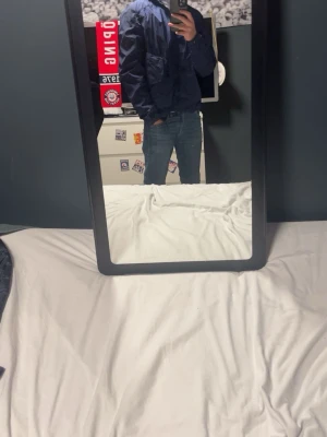 Blå Goggle Jacket från C.P. Company - Säljer en blå Goggle Jacket från C.P. Company i nylonmaterial. Jackan har huva, flera fickor framtill och klassiska guldiga tryckknappar. Snygg och sportig design med en loose passform, perfekt för dig som gillar streetwear.