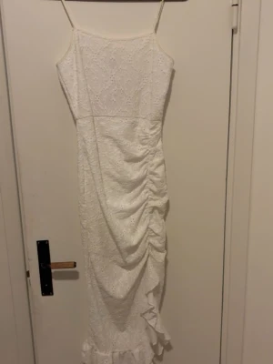 Vit spetsklänning med volang - Säljer en vit långklänning med smala axelband och vacker spets. Klänningen har omlottdetalj med rynk på sidan och volang längst ner. Perfekt för sommarens alla tillfällen! Den var köpt för min student men jag använde aldrig🥹 den är dock väldigt fin men känner att jag inte kommee ha användning för den. 