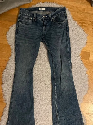 Blå bootcut jeans med broderade fickor - Säljer ett par blå bootcut jeans med snygga broderade detaljer på bakfickorna. Jeansen har klassisk femficksmodell, normal passform och är tillverkade i slitstarkt denim. Perfekta för dig som gillar en avslappnad men trendig look. 