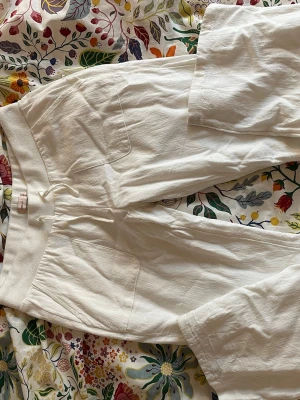 Vita linnebyxor med raka ben - Säljer ett par vita linnebyxor med raka ben och stora fickor framtill. Byxorna har en avslappnad passform och är perfekta för varma dagar. Materialet är linne vilket gör dem svala och sköna. Snygga att styla med en enkel topp eller skjorta.