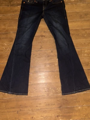 True Religion Joey Low Rise Flare Jeans - Mörkblå jeans från True Religion, modell Joey Low Rise Flare. Byxorna har tydliga kontrastsömmar, stora fickor bak med dekorativa knappar och klassisk True Religion-lapp. Flare-ben och låg midja ger en retrovibe. Materialet är klassisk jeansbomull. Pris kan diskuteras 💕💕