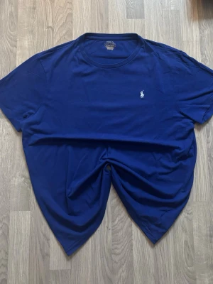 Blå t-shirt från Polo Ralph Lauren - Snygg blå t-shirt från Polo Ralph Lauren i custom slim fit. Klassisk design med korta ärmar och rund hals. Ikoniska vita broderade loggan på bröstet. Tillverkad i mjuk bomull som känns skön mot huden.                   Postat helst INTE med earlybird!!!