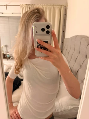 Vit omlottopp med drapering - Säljer en vit topp med snygg omlottdetalj och drapering framtill. Toppen har korta ärmar och är gjord i ett mjukt, stretchigt material som sitter skönt på kroppen. Perfekt för dig som gillar stilrena och trendiga plagg.