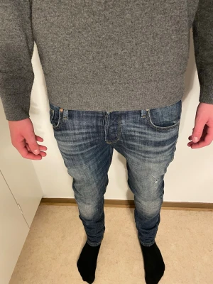 Blå jeans från Jack & Jones - Snygga blå jeans från Jack & Jones med slim passform och klassisk femficksdesign. Jeansen har slitningar och tvättad look, samt kontrastsömmar på bakfickorna. Materialet är jeans med en mjuk känsla och stretch för extra komfort.