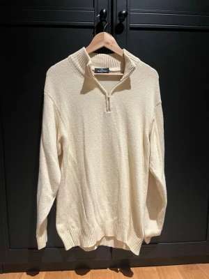 Vit half zip stickad tröja Valentino - Säljer en krämvit stickad tröja från Valentino med ribbad krage och half zip-dragkedja. Tröjan har långa ärmar, diskret broderad logga på ärmen och ribbade muddar. Perfekt för dig som gillar stilrena och klassiska plagg.