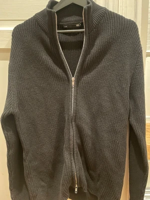 Mörkgrå stickad kofta med dragkedja - Mysig mörkgrå stickad kofta från 157 med hel dragkedja framtill och hög krage. Perfekt för lager på lager och chill dagar. Klassisk ribbstickad struktur och långärmad modell som passar till det mesta.