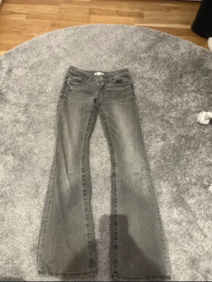 Grå bootcut jeans med fickdetaljer - Snygga grå bootcut jeans med coola fickdetaljer bak och knappar. Jeansen har låg midja och är tillverkade i mjukt denimtyg. Perfekta för dig som gillar en avslappnad men trendig look. Storlek 152