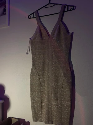 Glittrig beige kortklänning - Supersnygg beige så kallad ”bandage dress” med glittereffekt och breda axelband. Klänningen har v-ringning och markerade sömmar som ger en riktigt schysst passform. Dragkedja finns bak för enkel påklädning. Haft klänningen något år men aldrig används, därmed prislappen där bak. Säljer då den även är för stor för mig. Pris kan diskuteras.