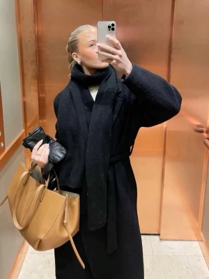 Svart lång kappa  - Sitter som S därmed stl!! Stilren svart kappa från InWear Premium med klassisk krage och knytskärp i midjan. Kappan har en rak och något oversized passform, perfekt för lager-på-lager. Tillverkad i ullblandning som håller dig varm under kyliga dagar. Be om bild på defekt vid intresse!