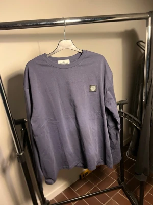  Stone Island - Långärmad tröja i lila från Stone Island med klassisk patch på bröstet. Tröjan har rund halsringning och är tillverkad i mjuk bomull. Perfekt för dig som gillar streetwear och vill ha en clean look.