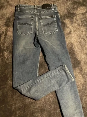  Nudie Jeans - Säljer ett par blå skinny jeans från Nudie Jeans med klassiska bakfickor och ljusa slitningar. Jeansen har normal midja och är tillverkade i mjukt denimtyg som sitter tajt längs benen. Perfekta för en avslappnad och trendig look.