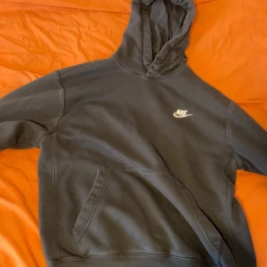 Svart Nike hoodie med vit logga - Svart hoodie från Nike med vit broderad logga på bröstet. Klassisk modell med stor huva och känguruficka framtill. Tillverkad i mjukt och bekvämt material, perfekt för en chill och sportig look.
