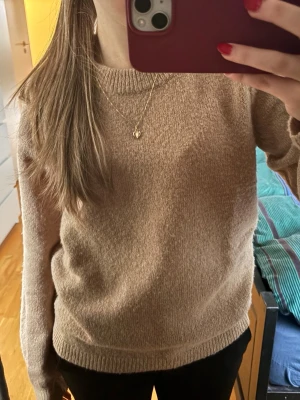 Beige stickad tröja med rund hals - Mysig beige stickad tröja med rund halsringning och långa ärmar. Tröjan har en enkel, klassisk design med ribbade muddar vid ärmslut och nederkant. Perfekt för lager på lager och passar till det mesta i garderoben.