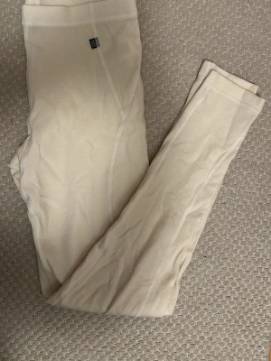 Beige tights från Pierre Robert - Mjuka och stretchiga underställs tights i vit från Helly Hansen. Tightsen har bred resår i midjan och synliga sömmar för extra komfort. Tillverkade i ett tunt och följsamt material som passar perfekt under kläder. Diskret logga vid midjan.