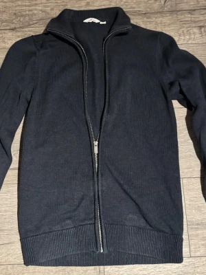 Mörkblå stickad ziptröja Dobber - Snygg mörkblå stickad tröja från Dobber med hel dragkedja framtill och hög krage. Tröjan har ribbade muddar vid ärmslut och nederkant, perfekt för lager på lager och en clean look.