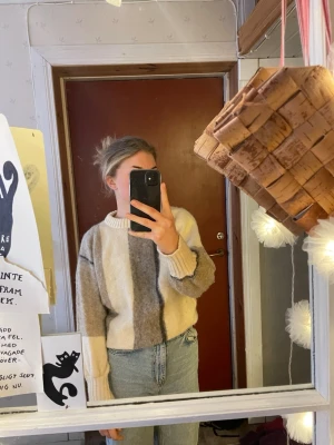 Beige och grå stickad tröja Icelandic - Mysig stickad tröja från The Icelander i ull med breda blockränder i beige, grått och offwhite. Tröjan har en avslappnad passform, rund hals och ribbade muddar vid ärmslut och nederkant. Perfekt för kalla dagar.