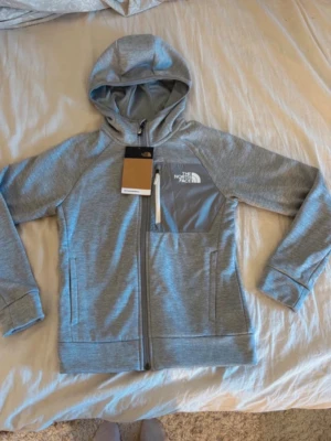 Grå hoodie från The North Face - Snygg grå hoodie från The North Face med dragkedja framtill och huva. Tröjan har en bröstficka med logga och detaljer i ljusare grått. Tillverkad av återvunnet material och har två sidofickor. Perfekt för chill dagar eller när du vill ha en sportig look.