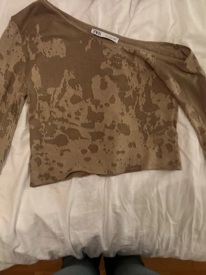 Beige croppad topp från Zara - Trendig croppad topp från Zara i beige med unikt camouflage-liknande mönster. Toppen har lång ärm och en bred, något offshoulder ringning. Dock är de ganska kort vilket gör att jag inte fått användning för den. Storlek s-m. Aldrig använd.