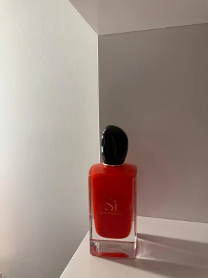 Giorgio Armani Sì röd parfymflaska  - Säljer en snygg parfym från Giorgio Armani, Sì, i en elegant röd glasflaska med svart lock. 100ml använd fåtal gånger. Perfekt för dig som gillar exklusiva dofter och vill ha en stilren flaska på hyllan.