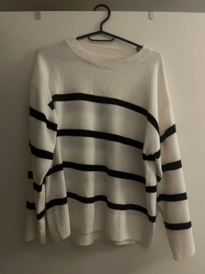 Vit och svart randig stickad tröja - Säljer en vit stickad tröja med svarta horisontella ränder. Tröjan har rund halsringning, långa ärmar och breda ribbade muddar vid ärmslut och nederkant. 