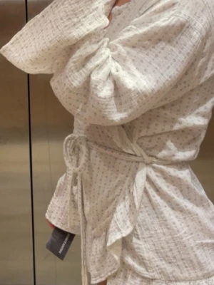 Morgonrock gina tricot  - Säljer en luftig vit morgonrock från gina tricot med små diskreta prickar, knytband i midjan och volangdetaljer längs kanten. Morgonrocken har en avslappnad passform 