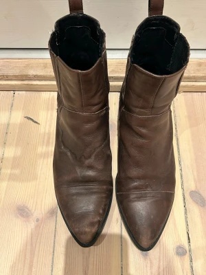 Bruna Vagabond chelsea boots i skinn - Säljer ett par bruna chelsea boots från Vagabond i storlek 41. Skorna är i skinn med spetsig tå, låg klack och elastiska paneler på sidorna. Klassisk och stilren modell som passar till många outfits. Perfekta för dig som gillar boots med lite edge.