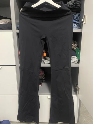 Svarta bootcut leggings - Säljer ett par svarta leggings med bootcut-modell och hög midja. De är tillverkade i ett stretchigt syntetmaterial som sitter skönt och följer kroppen. Perfekta för dig som gillar en enkel men trendig look.