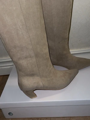 Boots Nelly - Snygga beige stövlar i mocka med spetsig tå och låg klack. Stövlarna har en stilren design och är perfekta för dig som vill ha en trendig look. Passar till både jeans och kjol för en cool vibe.