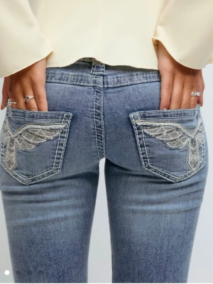 Blå bootcut jeans med broderade fickor - Snygga ljusblå bootcut jeans med broderade detaljer på bakfickorna och slitningar på benen. Jeansen har normal passform och är tillverkade i klassiskt denimtyg. Perfekta för dig som vill ha en cool och avslappnad look.