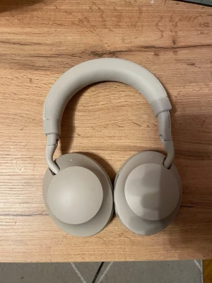 Feel 700ANC hörlurar  - Feel 700ANC trådlösa over-ear hörlurar i ljusgrå färg. Aktiv brusreducering, bekväm passform och modern design. Hörlurarna ser ut att vara i gott skick med minimalt slitage på kåpor och bygel. Perfekt för musik, resor och arbete.