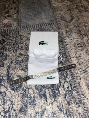 Lacoste Armband - Säljer ett stilrent och exklusivt armband från Lacoste i rostfritt stål. Armbandet består av eleganta rektangulära länkar där varannan länk pryds av Lacostes signaturmönster "Petit Piqué". En perfekt accessoar som kombinerar sportig elegans med en lyxig känsla.