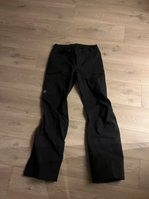 Svarta Arc'teryx täckbyxor dam S - Svarta skidbyxor från Arc'teryx för dam i storlek S. Byxorna har dragkedjor längs benen, justerbart bälte i midjan. Har ett litet litet jack där bak som jag täckt med en lapp. 
