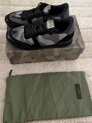 Valentino rockrunners - Snygga sneakers från Valentino Garavani i svart och grått med camouflagemönster. Skorna har snörning, rund tå och detaljer i mesh och skinn. Kommer med originalkartong och dustbag. Perfekta för dig som vill sticka ut med en exklusiv streetstyle.