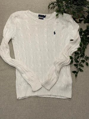 Vit kabelstickad tröja Polo Ralph Lauren - Kabelstickad vit tröja från Polo Ralph Lauren i mjuk pima bomull.   Klassisk rund hals, långärmad och med den ikoniska broderade loggan på bröstet. Perfekt till jeans ellerför en clean och tidlös look.   Storleken är S men passar som en Xs  Tveka inte att höra av dig om du har frågor 😊